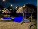 Night view of a tropical pool area with tiki huts and string lights at 262 Banana Rd, Palm Harbor, FL 34683