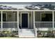 Close up of covered front porch features a stately blue door, steps with potted plants, and hanging plants at 5455 Lake Le Clare Rd, Lutz, FL 33558
