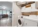 Well-lit laundry room with stackable washer and dryer, overhead cabinets, and a view of the living area at 10114 N Highland Ave, Tampa, FL 33612