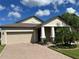 Tan house with beige garage door, landscaping, and palm trees at 13240 Satin Lily Dr, Riverview, FL 33579