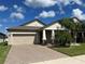 Tan house with beige garage door, landscaping, and palm trees at 13240 Satin Lily Dr, Riverview, FL 33579