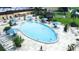 An aerial view showcases a large, oval-shaped pool with umbrella-covered tables and numerous lounge chairs for relaxing poolside at 2104 Hembury Pl # 33, Sun City Center, FL 33573