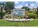 Welcoming Lake Tarpon Villas sign surrounded by lush landscaping and featuring the American flag at 2571 Cyprus Dr # 1-202, Palm Harbor, FL 34684