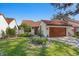 White stucco house with a brown tile roof, landscaped yard, and a wooden garage door at 11407 Robles Del Rio Pl, Temple Terrace, FL 33617