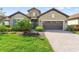 Charming home with a manicured lawn, stone accents, and a brick driveway leading to a two-car garage at 26810 Weiskopf Dr, Englewood, FL 34223