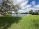 A beautiful lake view with a lush green lawn, mature tree, and cloud filled sky in backyard at 5195 Highbury Cir, Sarasota, FL 34238