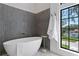 Bathroom featuring a modern freestanding tub with gray tiling, and a large window that showcases outside views at 4633 W Lowell Ave, Tampa, FL 33629