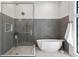 Bathroom featuring a modern glass-enclosed shower and freestanding tub with stylish gray and white tiling and window at 4633 W Lowell Ave, Tampa, FL 33629