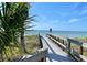 Picturesque view of beach access via wooden walkway, with palm trees and ocean in the distance at 3302 E Maritana Dr, St Pete Beach, FL 33706