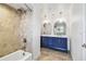 Modern bathroom featuring a blue double vanity, marble countertops, arch mirrors, and a tiled shower with a rainfall showerhead at 11683 Grove St, Seminole, FL 33772