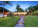 Landscaped backyard with a walkway, lighting, and tropical plants at dusk at 1560 53Rd N St, St Petersburg, FL 33710