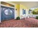 Inviting front porch with brick flooring, blue door, and classic white wicker chairs at 2501 Rustic Oaks Dr, Lutz, FL 33559