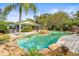 Beautiful backyard pool with mature landscaping, rock waterfall feature, and a covered outdoor living space at 2501 Rustic Oaks Dr, Lutz, FL 33559