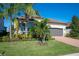 Landscaped one-story home with gray garage door and brick driveway, featuring palm trees and manicured lawn at 12241 Perennial Pl, Bradenton, FL 34211