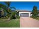 Single-story home with gray garage door and brick driveway, surrounded by palm trees and well-maintained lawn at 12241 Perennial Pl, Bradenton, FL 34211