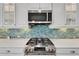 Modern kitchen with stainless steel gas range, microwave, white cabinets and blue mosaic tile backsplash at 721 Manns Harbor Dr, Apollo Beach, FL 33572