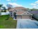 Two-story house with tan exterior, three-car garage, and manicured lawn at 2012 Fern Ridge Ct, Holiday, FL 34691
