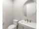 Modern powder room featuring a white toilet, sink, and a round mirror against a clean, light gray wall at 11971 Starbright Path, Venice, FL 34293