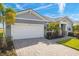 Charming gray home with a two-car garage, brick driveway, and beautifully landscaped front yard with palm trees at 11971 Starbright Path, Venice, FL 34293