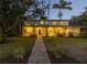 Charming home at dusk with a welcoming front walkway and lit windows, lush lawn, mature palm trees at 323 Coffee Pot Ne Dr, St Petersburg, FL 33704