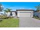 Charming single-story home featuring a gray two-car garage, paver driveway, manicured lawn, and tropical landscaping at 3065 Winding Creek Trl, North Port, FL 34289