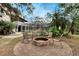 Outdoor brick fire pit with seating surrounded by lush landscaping and a screened pool in the background at 1406 Butch Cassidy Trl, Wimauma, FL 33598