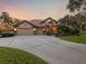 Home exterior at sunset with a three-car garage and lush landscaping at 3500 Woodridge Pl, Palm Harbor, FL 34684