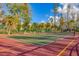 Outdoor tennis court surrounded by lush trees and greenery with well-maintained red and green surfaces at 4621 Gulf Of Mexico Dr # D10, Longboat Key, FL 34228