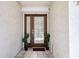 A brown paneled front door with sidelights is complemented by a ceramic tile entry and green decorative bushes at 273 Madeira Cir, Tierra Verde, FL 33715