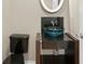 Stylish powder room featuring a black granite countertop with a unique blue vessel sink and black toilet at 10106 Radcliffe Dr, Tampa, FL 33626