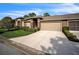 Exterior view of a tan two-car garage villa with a manicured lawn at 8015 Willow Brook Dr, Spring Hill, FL 34606