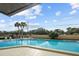 Community pool with palm trees, tables, chairs, and clear blue water on a sunny day with blue sky and light clouds at 2679 Sabal Springs Cir # 203, Clearwater, FL 33761