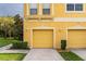 View of two townhouses with yellow siding, two-car garages, and manicured landscaping at 9042 Moonlit Meadows Loop, Riverview, FL 33578