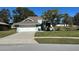 Charming light green house with a white garage door and manicured lawn at 1005 Lake Avoca Pl, Tarpon Springs, FL 34689