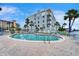 Community pool and seating area with lounge chairs next to a building under a clear blue sky at 18325 Gulf Blvd # 407, Redington Shores, FL 33708
