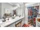 Bright bathroom featuring double sinks, white cabinetry, and a walk-in shower with a colorful curtain at 5215 New Brittany Ln, Zephyrhills, FL 33541
