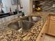 Double stainless steel sink with faucet set in granite countertop, complemented by mosaic tile backsplash and wood cabinetry at 12411 Cavalier Ct, Hudson, FL 34669