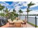 Cozy balcony with a wooden table set, a grill, and serene views of the water and palm trees at 16134 4Th E St, Redington Beach, FL 33708