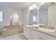 Bathroom with soaking tub, dual sinks, white cabinets, and arched mirrors at 4553 31St E Ct, Bradenton, FL 34203