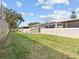Wide backyard with partial stucco wall, a screened-in lanai, and green grass, offering privacy at 1581 Amberlea S Dr, Dunedin, FL 34698