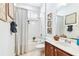 Bright bathroom featuring a shower-tub combo with white tiling, wood vanity, and decorative macrame art at 15005 Lake Emerald Blvd, Tampa, FL 33618