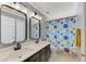 Well-lit bathroom with double sinks, dark gray cabinets, and a shower with floral curtains at 5608 Rockfield Loop, Valrico, FL 33596