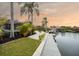 Beautiful waterfront property with a private dock, lush landscaping, and palm trees against a colorful sunset sky at 5809 Cruiser Way, Tampa, FL 33615