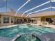 Screened-in pool featuring a hot tub, a bar area with stools, and tropical plants in a landscaped backyard with a clear sky at 12700 Grand Traverse Dr, Dade City, FL 33525