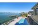 Aerial view showcasing a backyard pool, waterfront access, private dock, lounge chairs, and neatly trimmed palm trees at 26 Sunset Bay Drive, Belleair, FL 33756