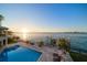 Backyard featuring a pool, dock, lounge chairs, palm trees, and waterfront views, offering a resort-like experience at 26 Sunset Bay Drive, Belleair, FL 33756