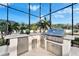 Built-in outdoor kitchen with a grill, mini fridge, and countertop space under a screened enclosure at 9401 93Rd St, Seminole, FL 33777