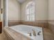 Close-up of tiled-in tub featuring elegant faucet, arched window and pillar in this well appointed bathroom at 1111 Carriage Park Dr, Valrico, FL 33594