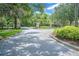 Secured gated entrance featuring stone pillars, lush greenery, and shade trees along winding drive at 15555 Martinmeadow Dr, Lithia, FL 33547