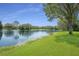 Beautiful pond view with a bright green grassy shoreline, and mature trees surrounding the water under a clear blue sky at 15555 Martinmeadow Dr, Lithia, FL 33547